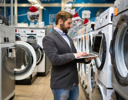 Medewerker van een elektronicaspeciaalzaak die tussen de wasmachines en laptops staat. Het i