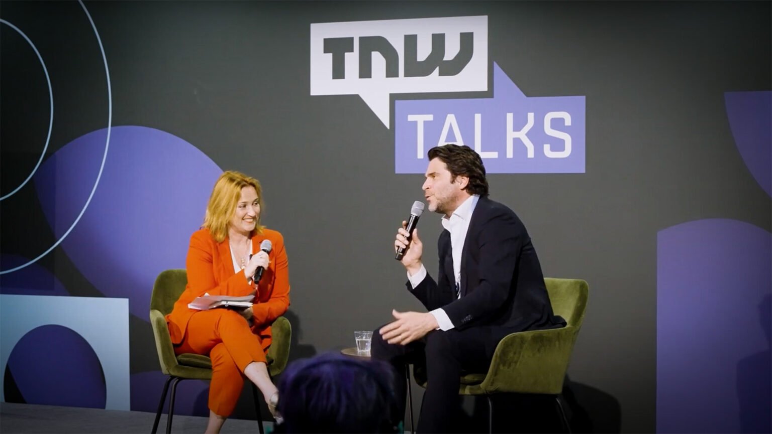 Xander de Buisonjé geinterviewd op The Next Web. Hij zit op een podium met een interviewster.